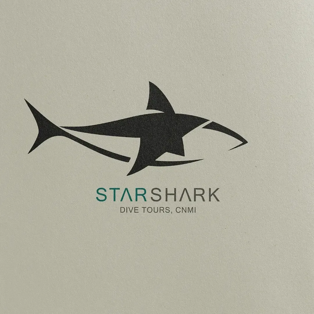 Starshark Dive Tours CNMI logo, a charcoal shark with a star cut into it above the teal and gray wordmark, printed on textured paper